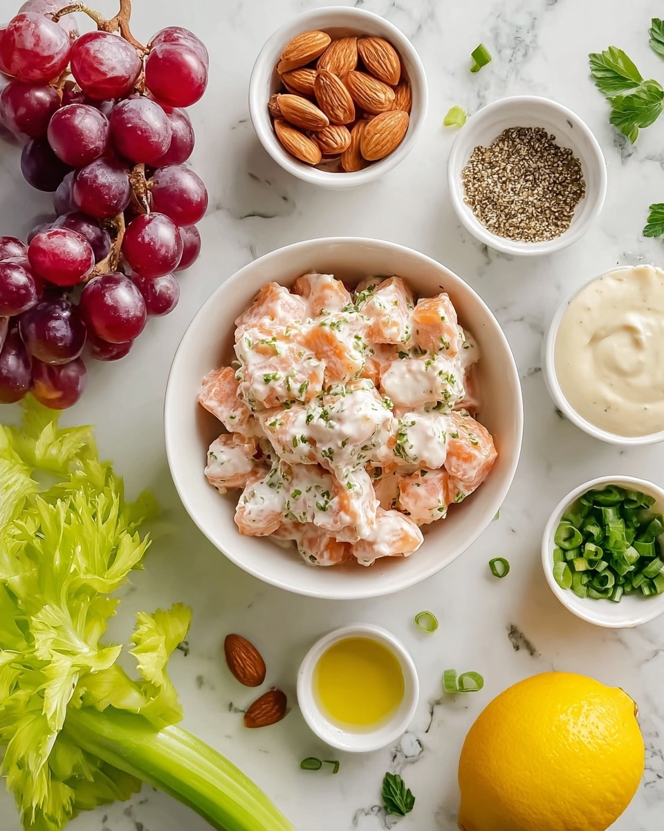 The image shows a white bowl filled with small, irregular pieces of light pink salmon mixed with a white creamy sauce sprinkled with green herbs, placed on a white marbled surface. Around this main bowl, there are smaller white dishes containing different ingredients: one with mixed whole almonds, another with a green and black spice blend, a third with a creamy sauce, and a fourth with a yellow oil. Fresh red grapes and green grapes on the vine sit next to the bowls, along with green celery sticks, a yellow lemon, some parsley sprigs, and a few sliced green onions scattered around. The scene is bright, clean, and fresh. photo taken with an iphone --ar 4:5 --v 7