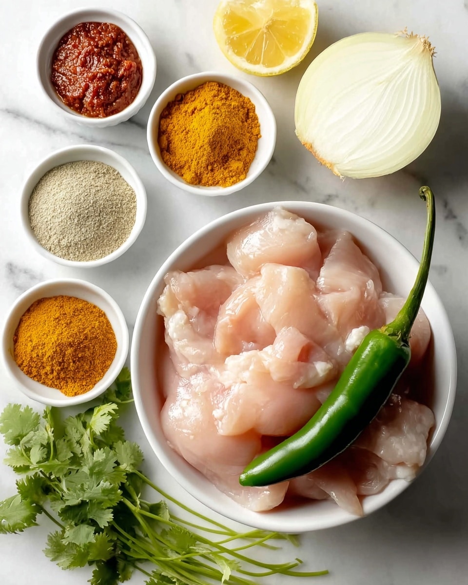 The image shows a white bowl filled with several pieces of raw, light pink chicken tenderloins with a shiny texture, placed at the bottom right. A fresh green chili pepper rests on top of the chicken. To the left of the bowl, there is a small bunch of fresh green cilantro leaves with thin stems lying on the white marbled surface. Surrounding the bowl are five small white ramekins, each containing different ingredients: at the top left is a reddish-brown thick paste, below it is a beige powder, next is a bright yellow-orange powder, then a golden yellow liquid, and finally a light grayish powder at the top right. Above the bowl to the right is a halved white onion with a smooth cut side facing up, and next to it is a halved lemon with the bright yellow flesh visible. The background is a white marbled texture. Photo taken with an iphone --ar 4:5 --v 7