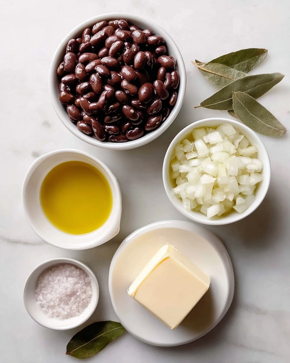 The image shows five small white bowls and plates arranged on a white marbled surface, each holding a different ingredient. At the top left is a bowl filled with shiny dark brown beans, smooth and round, tightly packed. Below it is a bowl with small diced white onion pieces, translucent and fresh-looking. To the right of the beans, a small bowl contains golden yellow olive oil with a smooth surface. Below the oil, on a small white round plate, lies a square block of creamy white butter with smooth edges. Finally, in the bottom left corner, a tiny bowl holds coarse white salt crystals. Two dried green leaves are placed next to the olive oil bowl. photo taken with an iphone --ar 4:5 --v 7