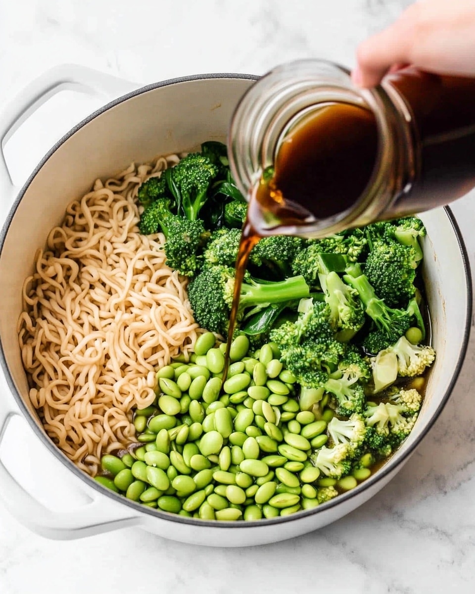 A white bowl filled with three layers of food: the first layer has bright green edamame beans and pieces of green vegetables, the second layer shows curly golden brown noodles mixed with the vegetables, and the top layer is sprinkled with white sesame seeds and red chili flakes, giving a textured and colorful topping. The bowl is placed on a white marbled surface with two small blurry bowls in the background, one with green garnish. photo taken with an iphone --ar 4:5 --v 7